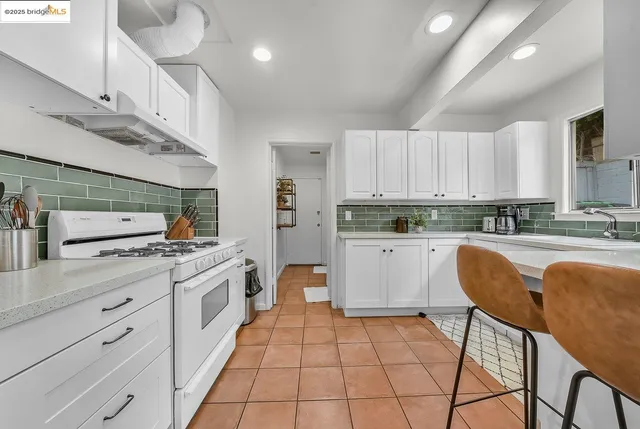 a kitchen with stainless steel appliances granite countertop a stove a sink dishwasher and white cabinets with wooden floor