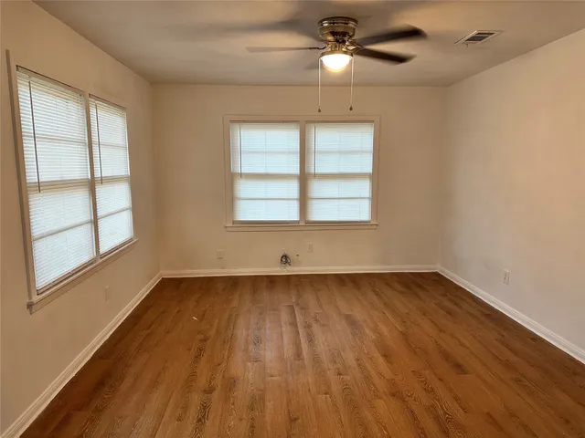 an empty room with wooden floor chandelier fan and windows