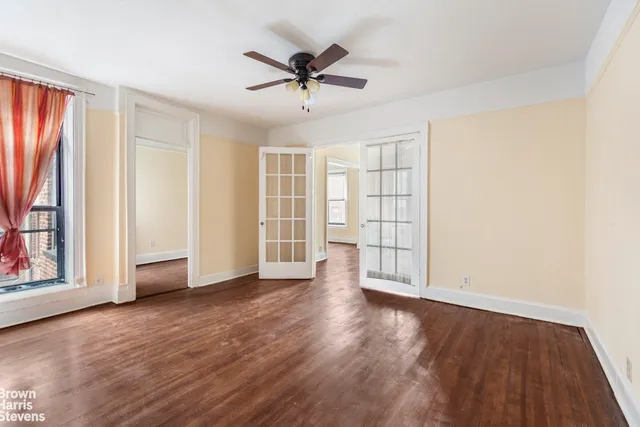 an empty room with wooden floor chandelier fan and windows