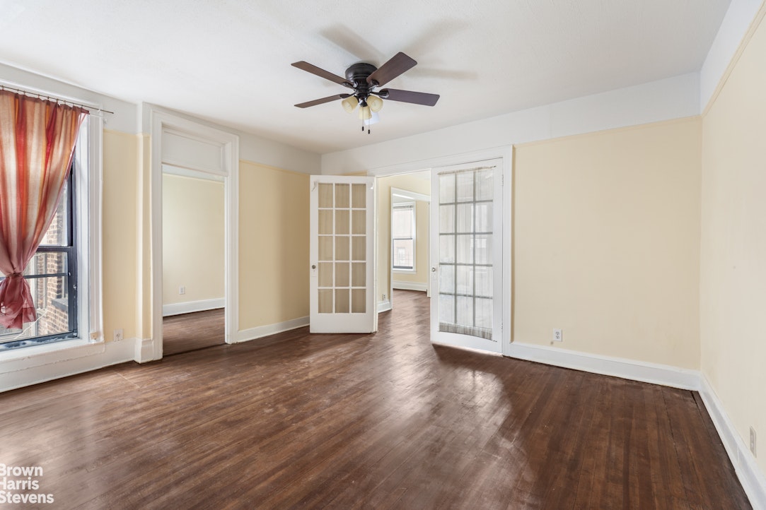 an empty room with wooden floor chandelier fan and windows