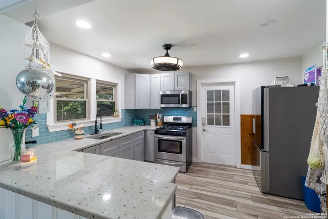 a kitchen with stainless steel appliances granite countertop a refrigerator a sink dishwasher a stove and a dining table with wooden floor