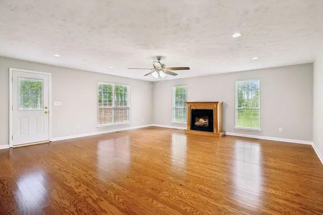 an empty room with wooden floor fireplace and windows