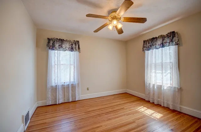 an empty room with wooden floor chandelier fan and windows