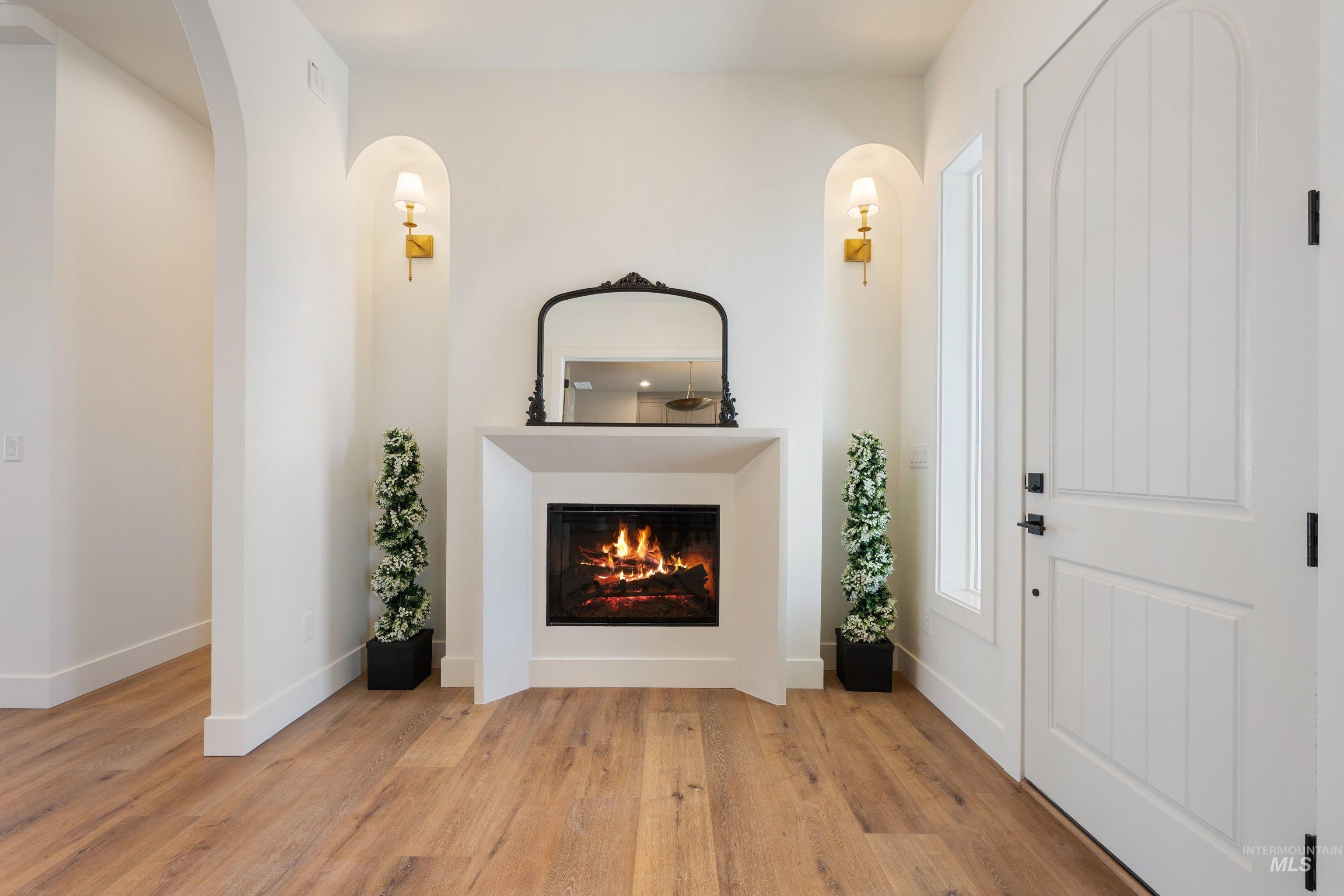 24821 Ardmore Court Caldwell, ID 83607 - Photo 7 of 43 Entryway featuring a fireplace with a stone-finish mantel, wood-finish flooring, an arched doorway, and an arched entry door with a sidelight