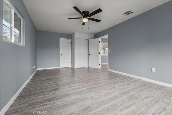 a view of an empty room with wooden floor and a ceiling fan
