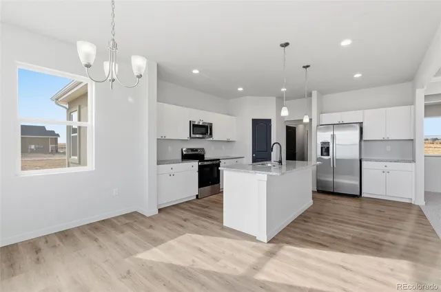 a large kitchen with kitchen island a refrigerator a stove a sink dishwasher a oven with white cabinets and wooden floor