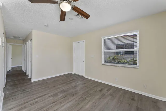 a view of an empty room with wooden floor and a ceiling fan
