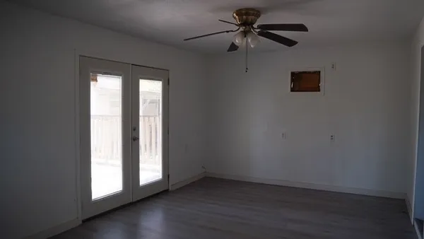 an empty room with wooden floor fan and windows