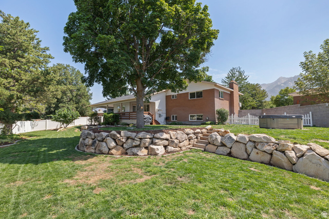2370 Quail Run Circle East Sandy, UT 84093 - Photo 40 of 54 Expansive backyard featuring a tiered landscape with a rock retaining wall, mature trees, and a covered porch