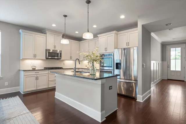 a kitchen with stainless steel appliances granite countertop a refrigerator a sink dishwasher a stove and white cabinets with wooden floor