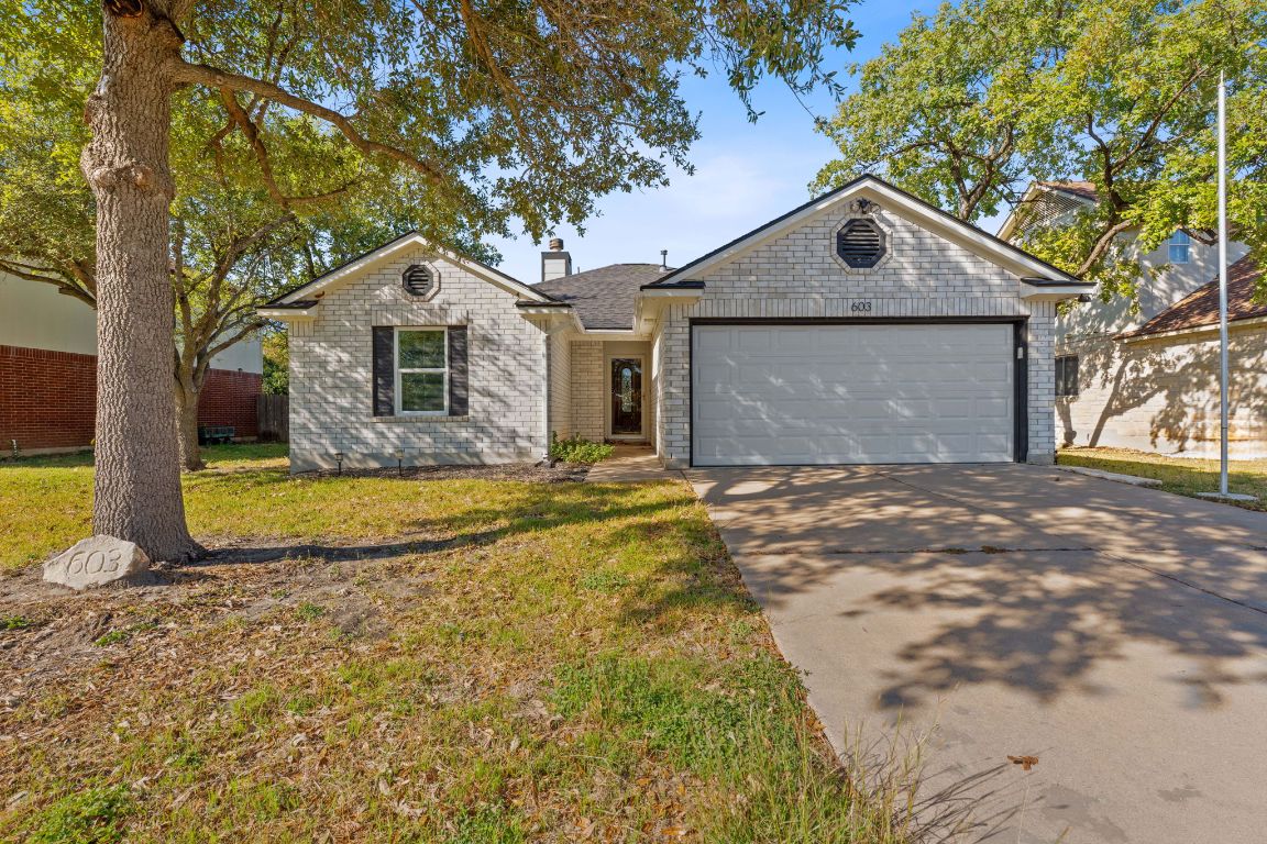 Ranch-style house featuring concrete driveway, a front yard, a chimney, an attached garage, and brick siding