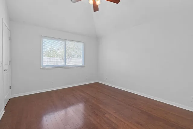 an empty room with wooden floor chandelier fan and windows