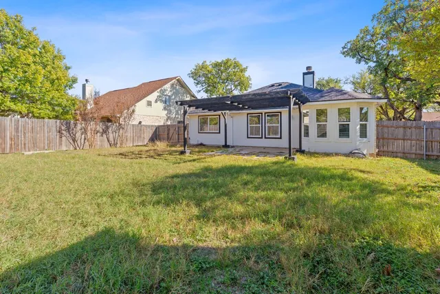 a white house with a big yard and large trees with wooden fence