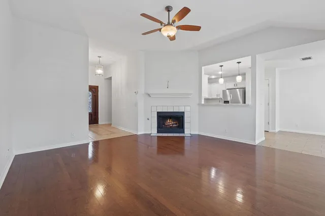 an empty room with wooden floor a ceiling fan a fireplace and windows in a room