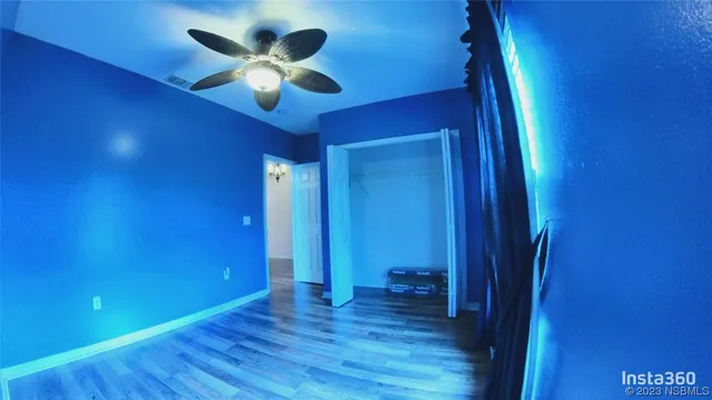 a view of an empty room with wooden floor and a ceiling fan