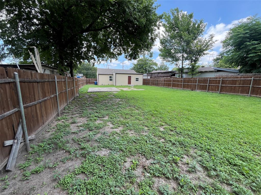 7046 Forney Road Dallas, TX 75227 - Photo 19 of 19 Expansive backyard with a wood privacy fence, featuring a detached shed with a neutral-toned exterior, a red door, and a single window