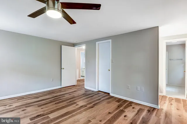an empty room with wooden floor ceiling fan and windows