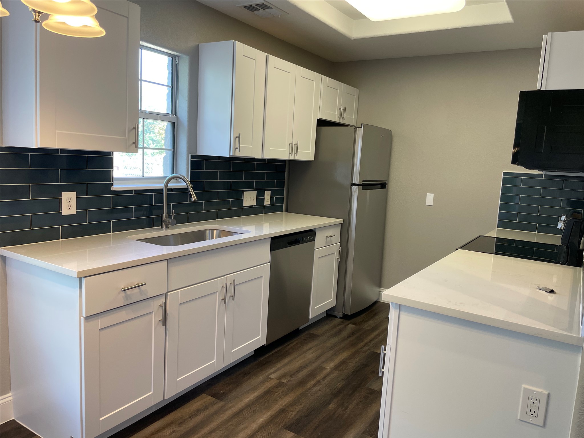 2004 Maple Street Georgetown, TX 78626 - Photo 11 of 31 Kitchen featuring white shaker cabinetry, light-toned countertops, a dark subway tile backsplash, stainless steel appliances, and wood-finish flooring