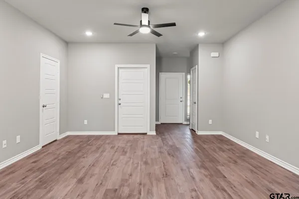 an empty room with wooden floor ceiling fan and windows