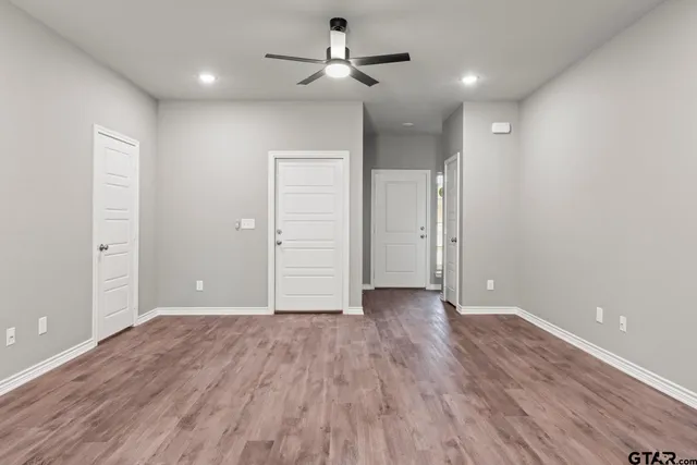 an empty room with wooden floor ceiling fan and windows