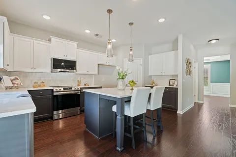 a kitchen with stainless steel appliances granite countertop a stove top oven a refrigerator a sink a dining table and chairs with wooden floor