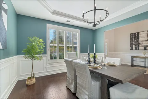 a dining room with wooden floor a chandelier a glass table and chairs