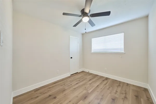 an empty room with wooden floor fan and windows