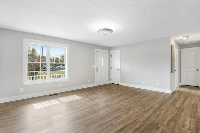a view of an empty room with wooden floor and a window