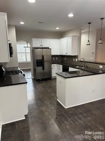 a kitchen with granite countertop a refrigerator a sink and white cabinets