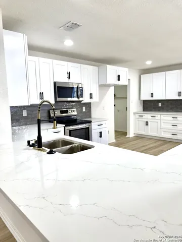 a kitchen with stainless steel appliances granite countertop a stove top oven a sink and white cabinets