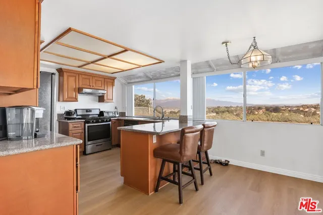 a kitchen with stainless steel appliances kitchen island granite countertop a stove a refrigerator a sink a dining table and chairs with wooden floor