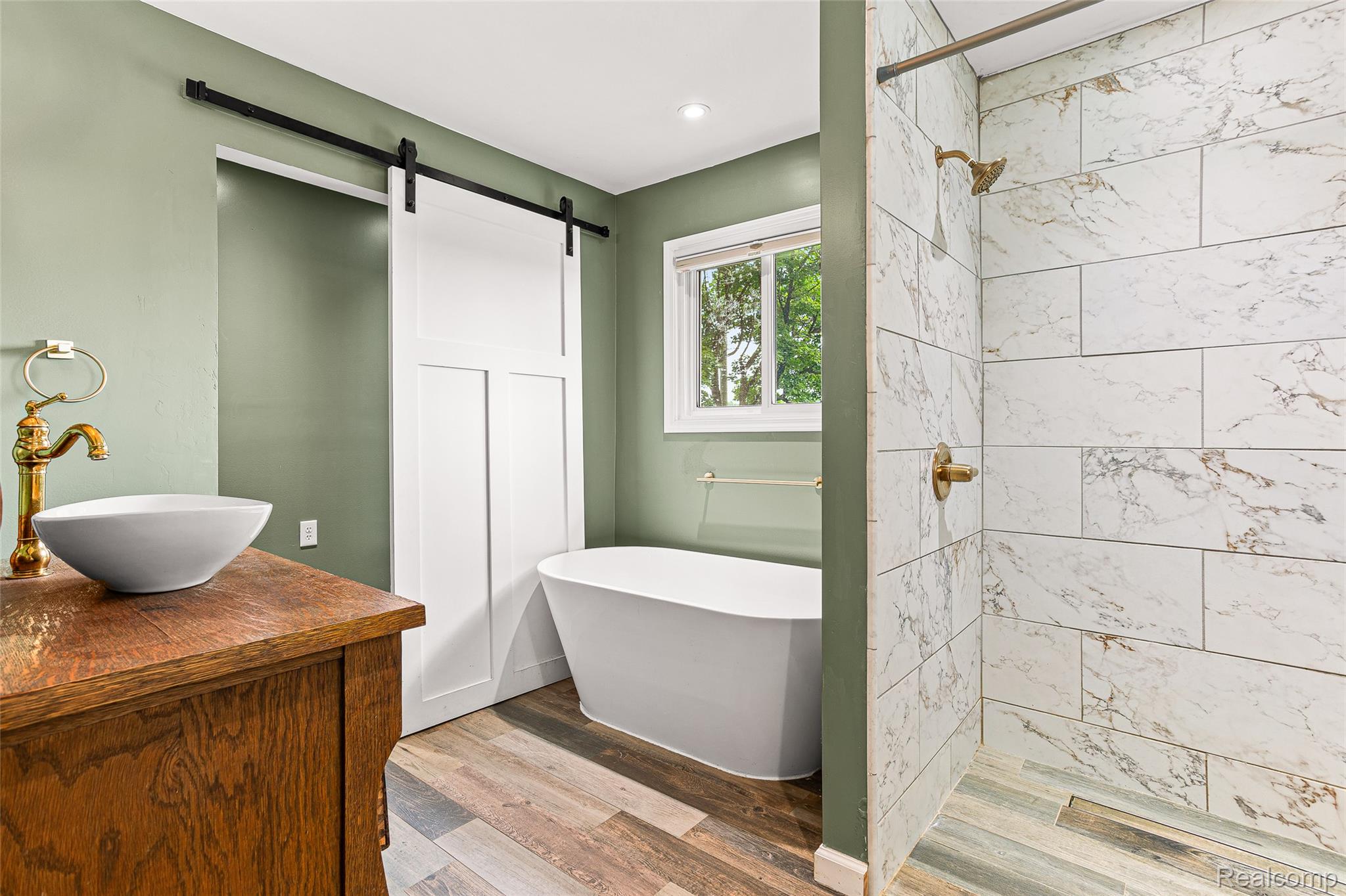 9561 Exeter Road Carleton, MI 48117 - Photo 21 of 46 Freestanding soaking tub, walk-in shower with large format tile, wood-finish flooring, wood vanity, and a vessel sink with brass-finish faucet