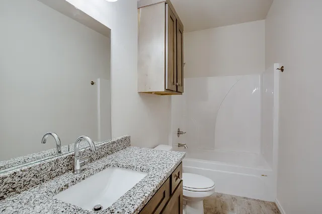 a bathroom with a granite countertop sink a toilet and shower
