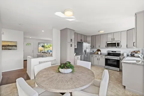 a kitchen with stainless steel appliances kitchen island granite countertop a refrigerator a stove a sink a dining table and chairs with wooden floor