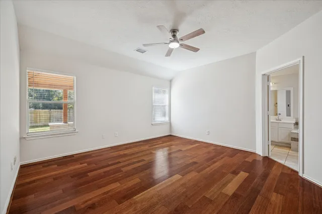 a view of an empty room with wooden floor and a ceiling fan