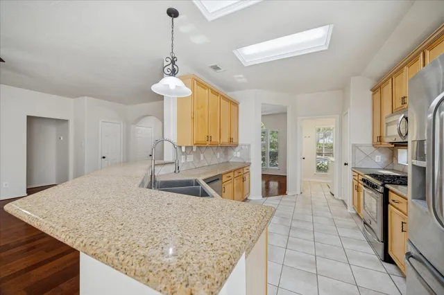 a large kitchen with stainless steel appliances granite countertop a stove top oven a sink dishwasher a dining table and chairs with wooden floor