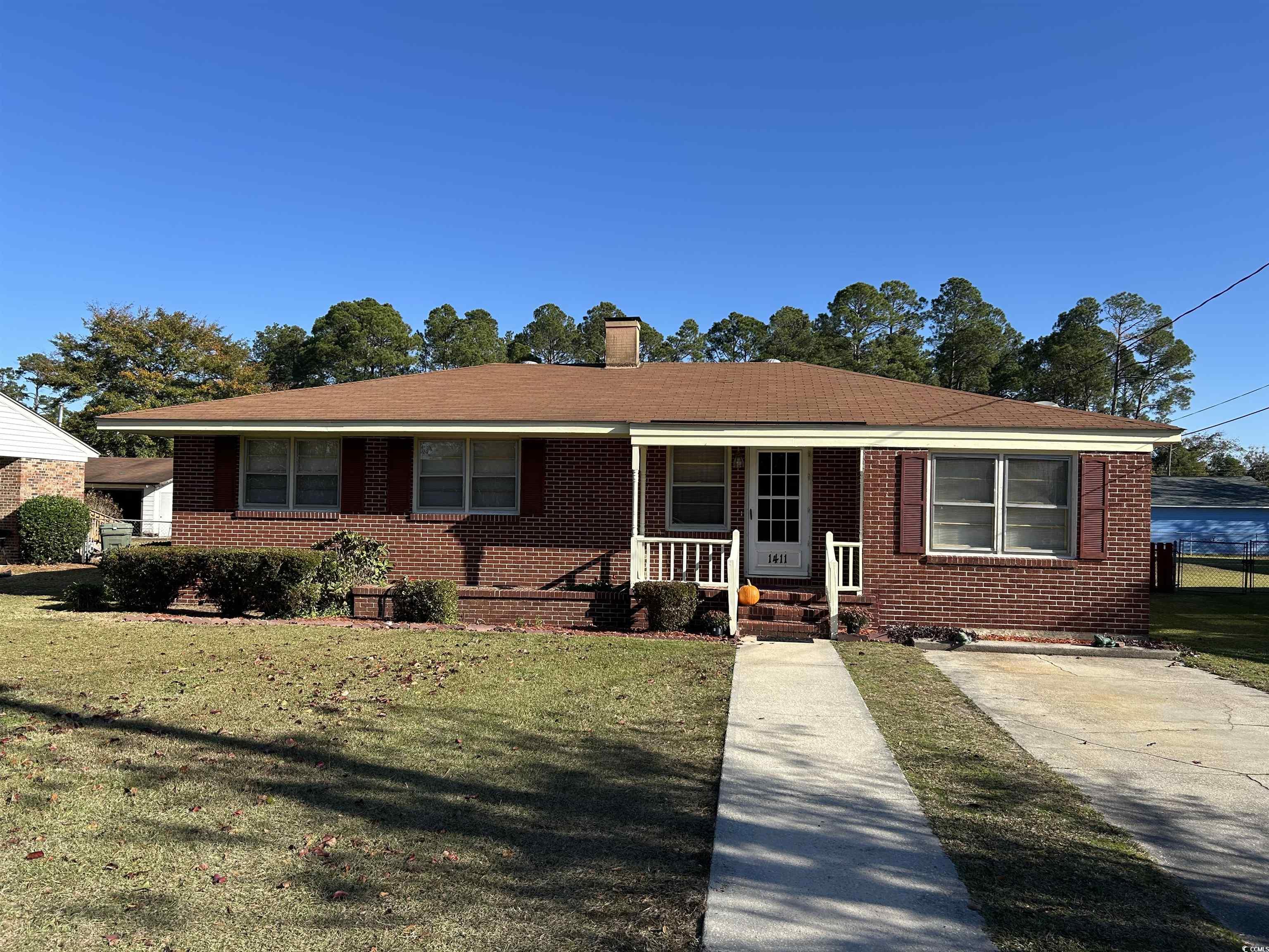 View of front of home with a front lawn, brick siding, a porch, and a chimney