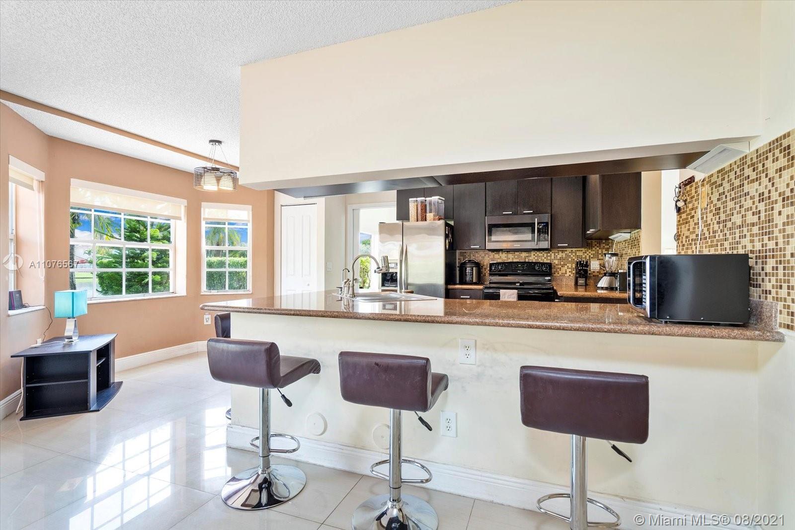 153 Granada Avenue Weston, FL 33326 - Photo 13 of 37 a kitchen with stainless steel appliances granite countertop a stove a sink a microwave a refrigerator and chairs