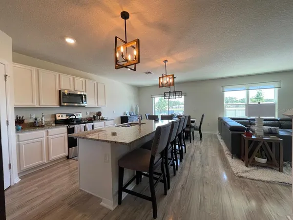 a open kitchen with stainless steel appliances granite countertop a stove a refrigerator a kitchen island a dining table and chairs with wooden floor