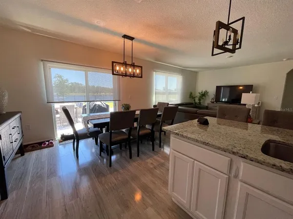 a open kitchen with stainless steel appliances granite countertop a dining table chairs stove a refrigerator and chandelier