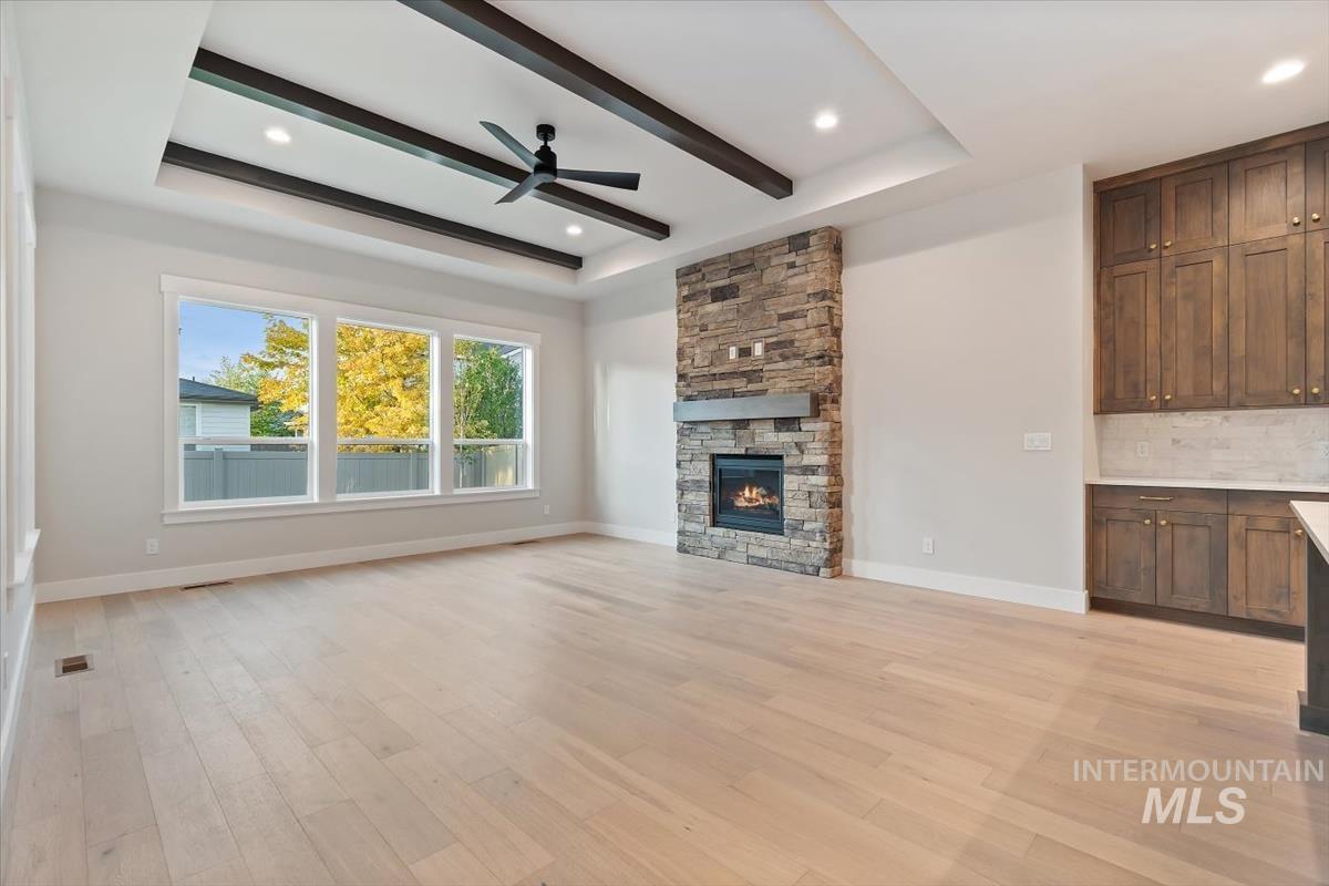 2147 East Blakehurst Avenue Kuna, ID 83634 - Photo 7 of 43 Unfurnished living room featuring a fireplace, beam ceiling, light wood-type flooring, ceiling fan, and a tray ceiling