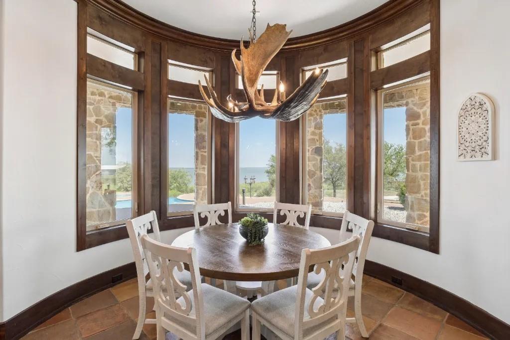 1180 McReynolds Road Sanger, TX 76266 - Photo 12 of 40 Curved window wall with dark wood trim, stone exterior accents visible through windows, and a sculptural antler-style chandelier