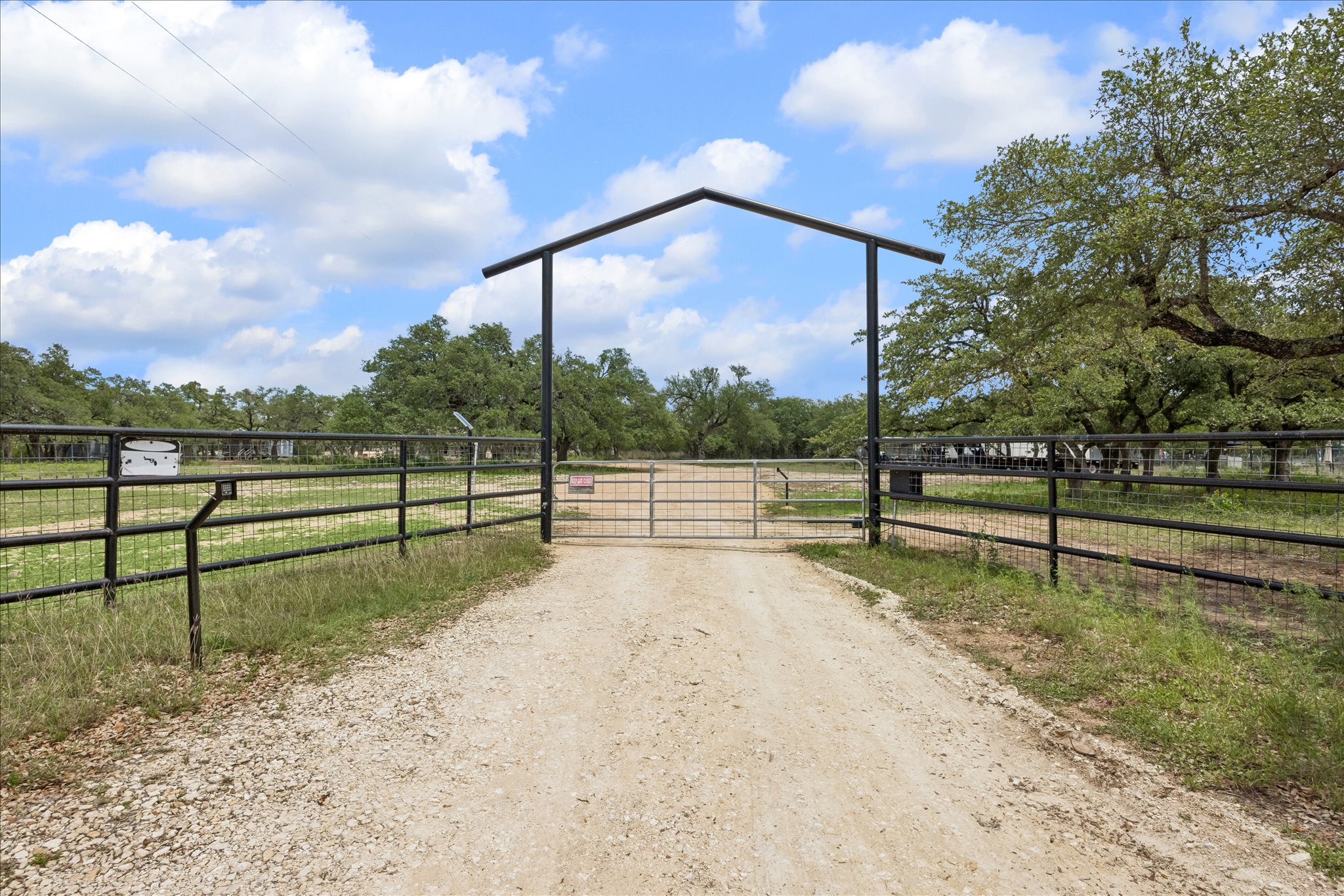 6411 West Fitzhugh Road Dripping Springs, TX 78620 - Photo 31 of 34 Gravel driveway entry with a black metal archway and matching perimeter fencing