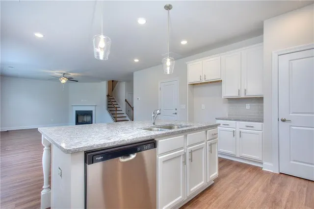 a kitchen with a sink dishwasher and white cabinets with wooden floor