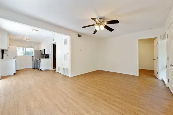 a view of an empty room with wooden floor and a kitchen
