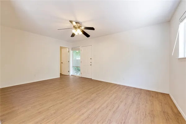 an empty room with wooden floor ceiling fan and windows