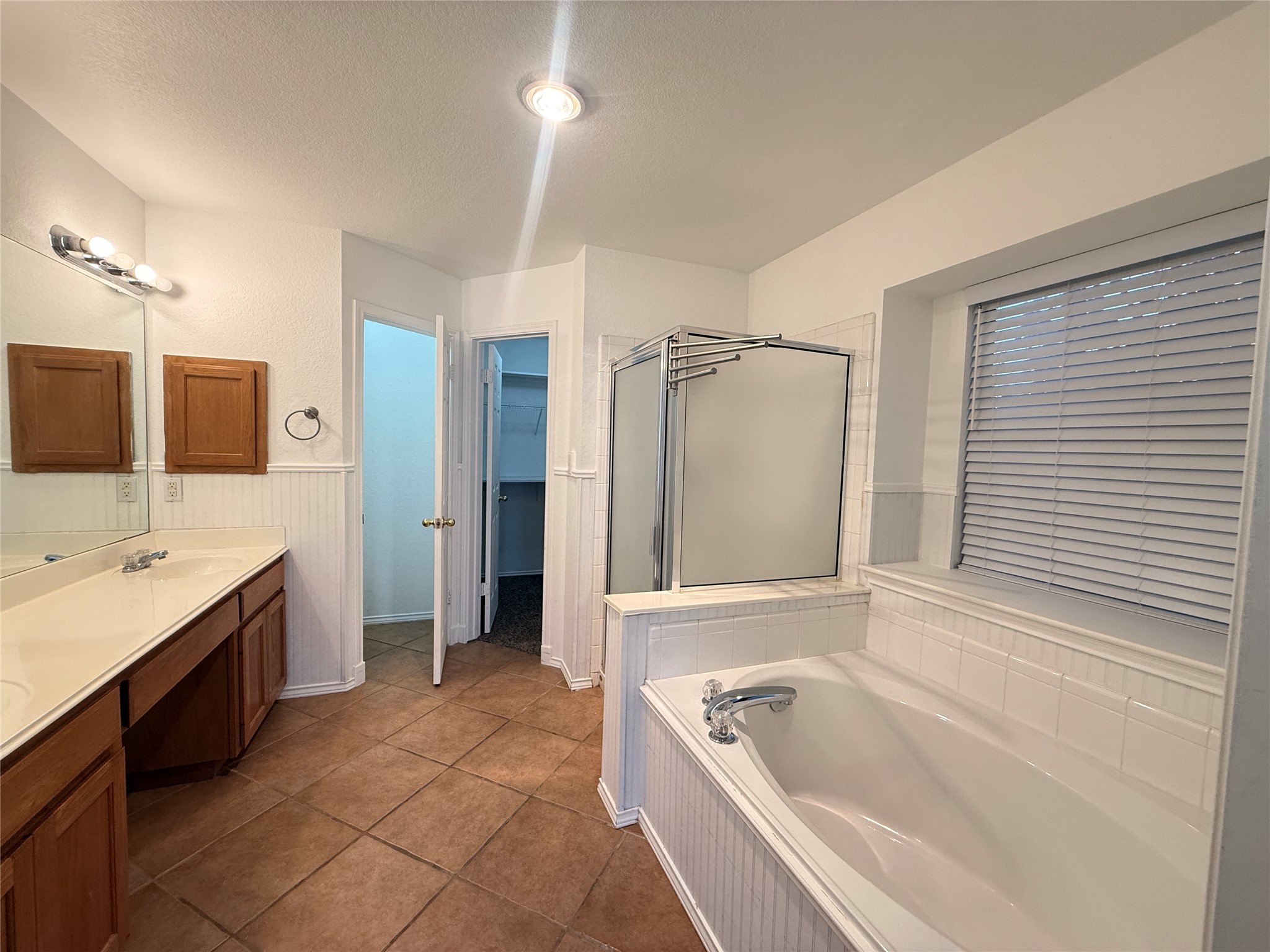 708 Spring Brook Lane Leander, TX 78641 - Photo 13 of 27 Bathroom featuring a shower stall, double vanity, a textured ceiling, wainscoting, and dark tile patterned flooring