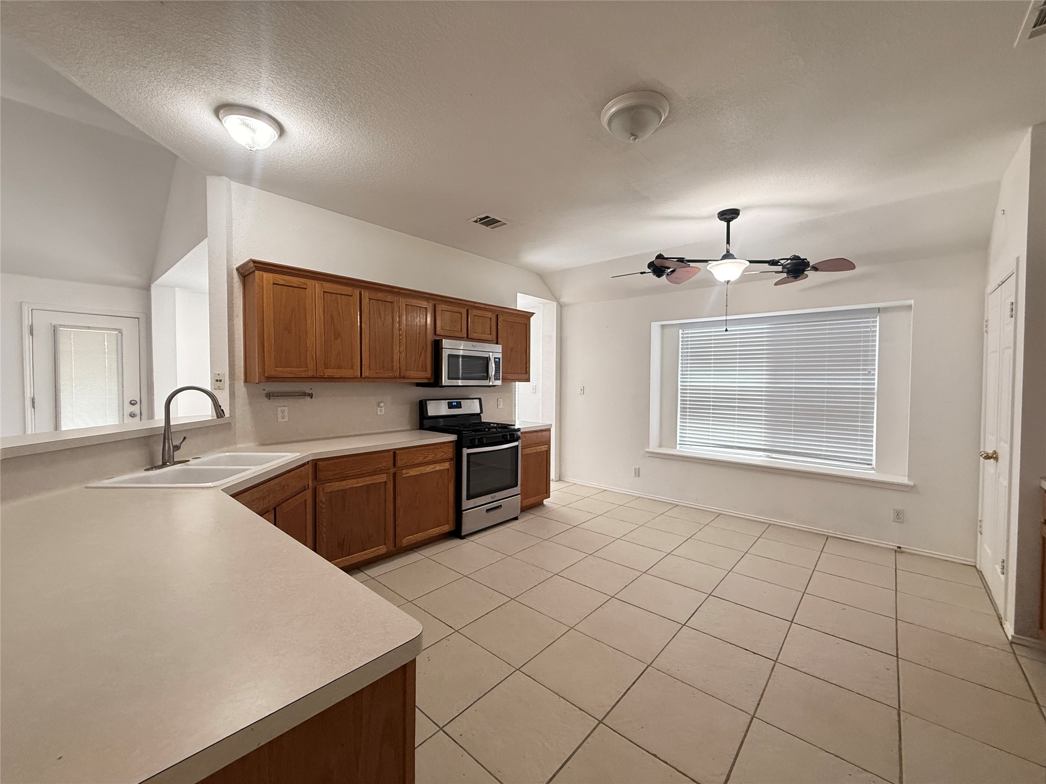 708 Spring Brook Lane Leander, TX 78641 - Photo 8 of 27 Kitchen with stainless steel appliances, wood finish cabinets, light countertops, light tile patterned floors, and a ceiling fan