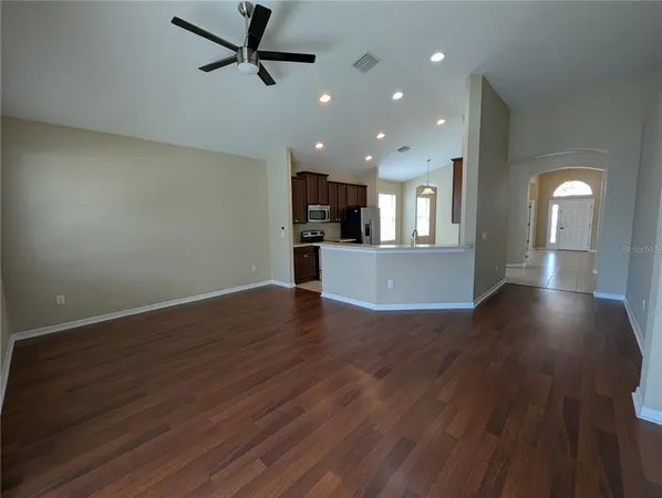 a view of an empty room with wooden floor and a ceiling fan