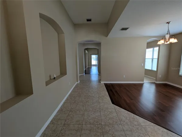 an empty room with wooden floor chandelier and windows